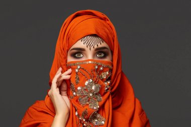 Payetler ve takılar ile süslenmiş terracotta hijab giyen genç bir büyüleyici kadın stüdyo çekim. Arap tarzı.