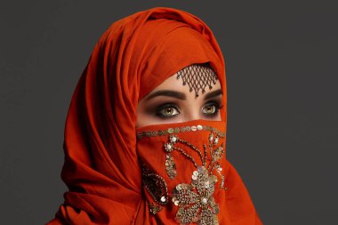 Payetler ve takılar ile süslenmiş terracotta hijab giyen genç bir büyüleyici kadın stüdyo çekim. Arap tarzı.