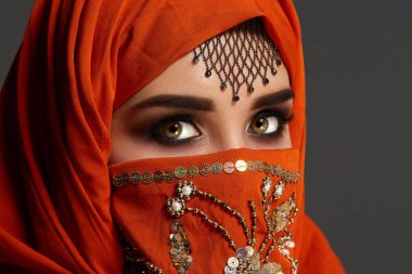Payetler ve takılar ile süslenmiş terracotta hijab giyen genç bir büyüleyici kadın stüdyo çekim. Arap tarzı.