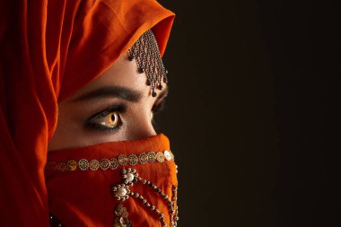 Payetler ve takılar ile süslenmiş terracotta hijab giyen genç bir büyüleyici kadın stüdyo çekim. Arap tarzı.