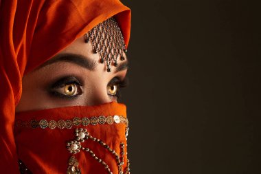 Payetler ve takılar ile süslenmiş terracotta hijab giyen genç bir büyüleyici kadın stüdyo çekim. Arap tarzı.