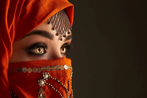 Payetler ve takılar ile süslenmiş terracotta hijab giyen genç bir büyüleyici kadın stüdyo çekim. Arap tarzı.