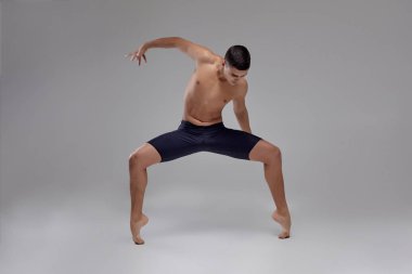 Yakışıklı bir adam bale dansçısı fotoğraf, siyah şort giymiş, stüdyoda gri bir arka plan karşı bir dans unsuru yapma.