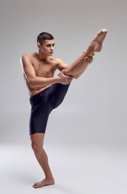 Yakışıklı bir adam bale dansçısı fotoğraf, siyah şort giymiş, stüdyoda gri bir arka plan karşı bir dans unsuru yapma.