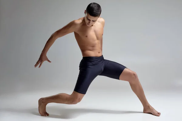 Foto de um homem bonito bailarino de balé, vestido com shorts pretos, fazendo um elemento de dança contra um fundo cinza no estúdio . — Fotografia de Stock