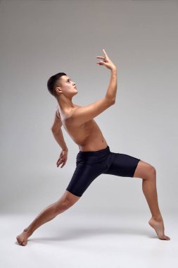 Yakışıklı bir adam bale dansçısı fotoğraf, siyah şort giymiş, stüdyoda gri bir arka plan karşı bir dans unsuru yapma.