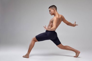 Yakışıklı bir adam bale dansçısı fotoğraf, siyah şort giymiş, stüdyoda gri bir arka plan karşı bir dans unsuru yapma.