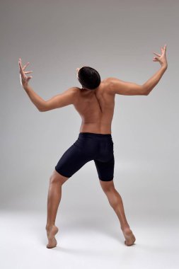 Yakışıklı bir adam bale dansçısı fotoğraf, siyah şort giymiş, stüdyoda gri bir arka plan karşı bir dans unsuru yapma.