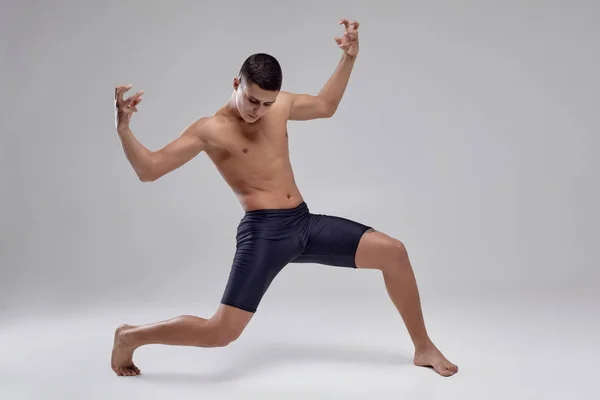 Photo of a handsome man ballet dancer, dressed in a black shorts, making a dance element against a gray background in studio. — Stock Photo, Image