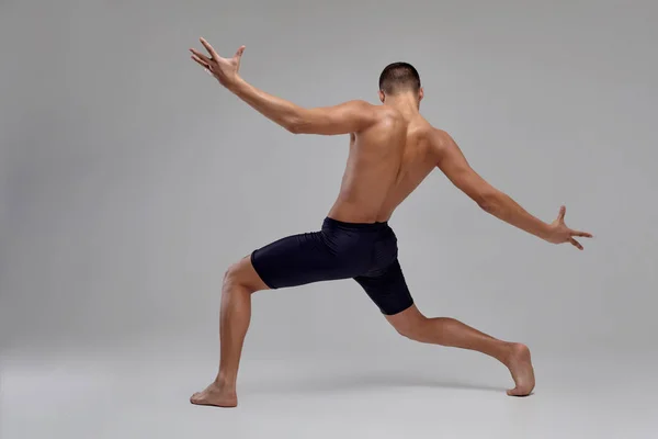 Foto de un hombre guapo bailarín de ballet, vestido con pantalones cortos negros, haciendo un elemento de baile sobre un fondo gris en el estudio . —  Fotos de Stock