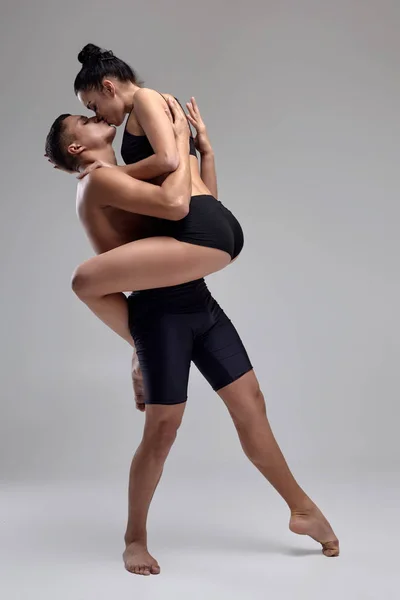 Το ζευγάρι ενός νεαρού σύγχρονου χορού μπαλέτου με μαύρα κοστούμια ποζάρει σε ένα γκρίζο φόντο στούντιο. — Φωτογραφία Αρχείου