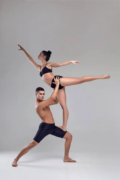 O casal de jovens bailarinos modernos em ternos pretos estão posando sobre um fundo de estúdio cinza . — Fotografia de Stock