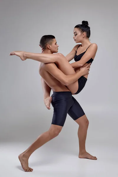 O casal de jovens bailarinos modernos em ternos pretos estão posando sobre um fundo de estúdio cinza . — Fotografia de Stock