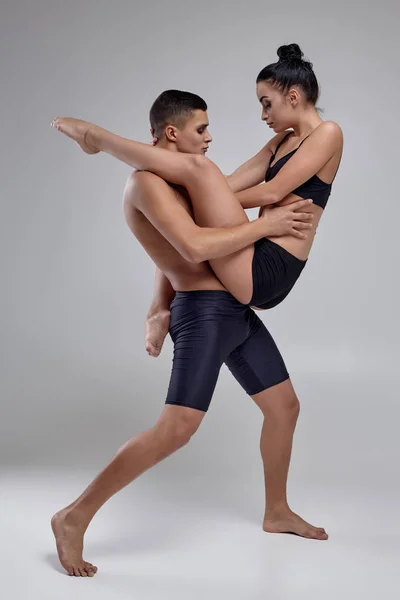 O casal de jovens bailarinos modernos em ternos pretos estão posando sobre um fundo de estúdio cinza . — Fotografia de Stock