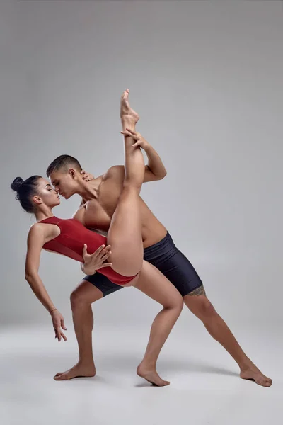 The couple of an athletic modern ballet dancers are posing against a gray studio background. — Stock Photo, Image