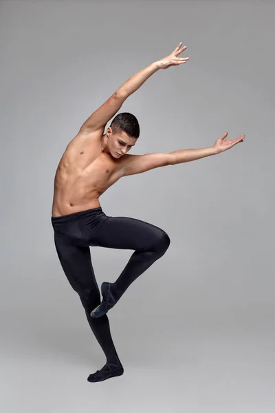 Foto de um atlético dançarino de balé, vestido com uma meia-calça preta e ponteiro, fazendo um elemento de dança contra um fundo cinza em estúdio . — Fotografia de Stock