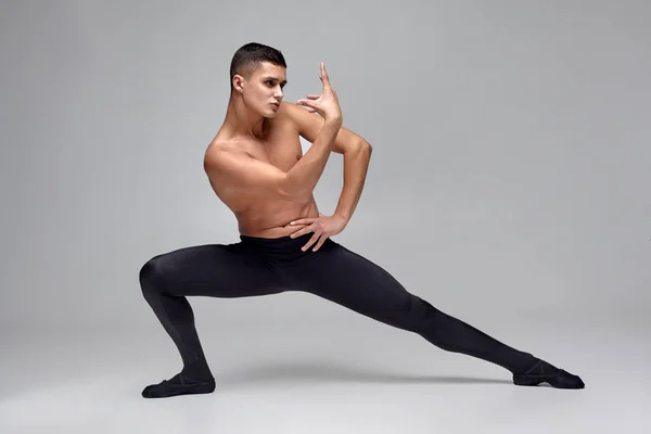 Foto de um atlético dançarino de balé, vestido com uma meia-calça preta e ponteiro, fazendo um elemento de dança contra um fundo cinza em estúdio . — Fotografia de Stock