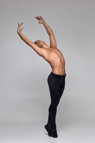 Foto van een atletische man ballet danser, gekleed in een zwarte panty's en Pointe, het maken van een dans element tegen een grijze achtergrond in Studio. — Stockfoto