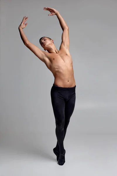 Photo d'un danseur de ballet homme athlétique, vêtu d'un collant noir et pointe, faisant un élément de danse sur un fond gris en studio . — Photo
