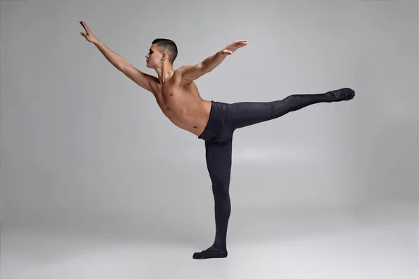 Foto van een atletische man ballet danser, gekleed in een zwarte panty's en Pointe, het maken van een dans element tegen een grijze achtergrond in Studio. — Stockfoto