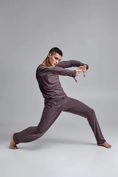 Foto van een atletische man ballet danser gekleed in een grijze trainingspak, het maken van een dans element tegen een grijze achtergrond in Studio. — Stockfoto