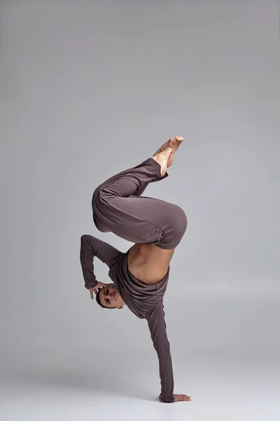 Fotografie atletického baletního tanečníka v šedém teplákovém obleku, který v ateliéru dělá taneček na šedé pozadí. — Stock fotografie