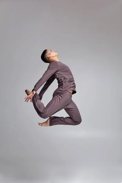 Gri eşofman giymiş bir atletik adam bale dansçısı Fotoğraf, stüdyoda gri bir arka plan karşı bir dans unsuru yapma. — Stok fotoğraf