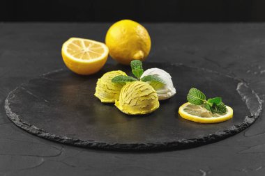 Nane ile süslenmiş lezzetli krem ve limonlu dondurma siyah bir arka plan üzerinde bir taş kayrak üzerinde servis.