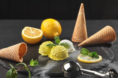 Siyah bir arka plan üzerinde bir taş kayrak üzerinde duman servis nane ile süslenmiş lezzetli krem ve limon dondurma.