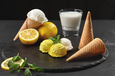 Nane ile süslenmiş lezzetli krem ve limonlu dondurma siyah bir arka plan üzerinde bir taş kayrak üzerinde servis.