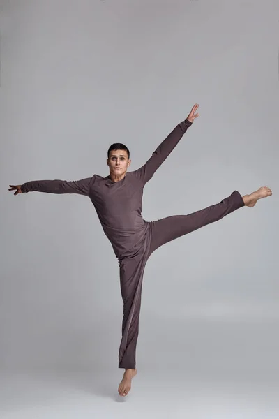 Photo d'un danseur de ballet homme athlétique vêtu d'un survêtement gris, faisant un élément de danse sur un fond gris en studio . — Photo