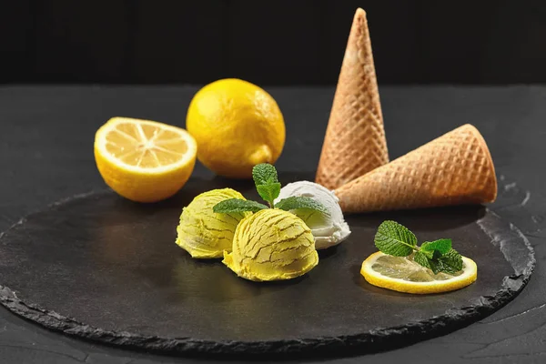 Tasty creamy and lemon ice cream decorated with mint served on a stone slate over a black background.