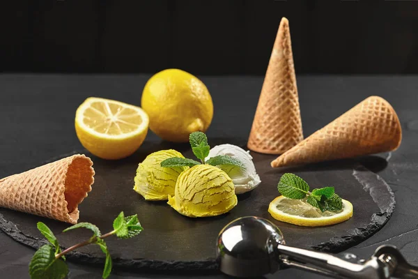 Tasty creamy and lemon ice cream decorated with mint served on a stone slate over a black background. — Stock Photo, Image