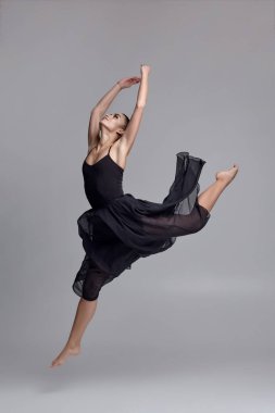 Siyah elbiseli dans eden balerin. Gri arka planda çağdaş zarif performans.