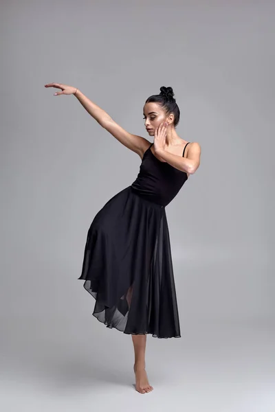 Ballerine dansante en robe noire. Performance gracieuse contemporaine sur fond gris . — Photo