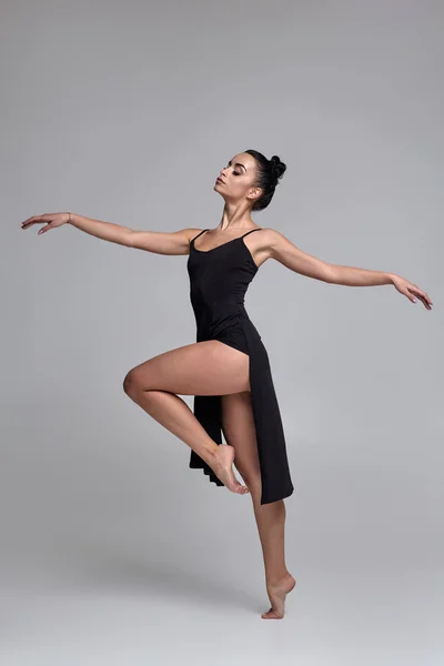 Dansen ballerina in een zwarte jurk. Eigentijdse sierlijke prestaties op een grijze achtergrond. — Stockfoto