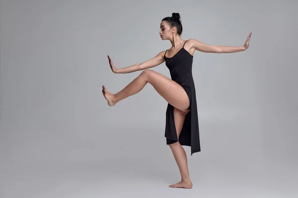 Dancing ballerina in a black dress. Contemporary graceful performance on a gray background. — Stock Photo, Image