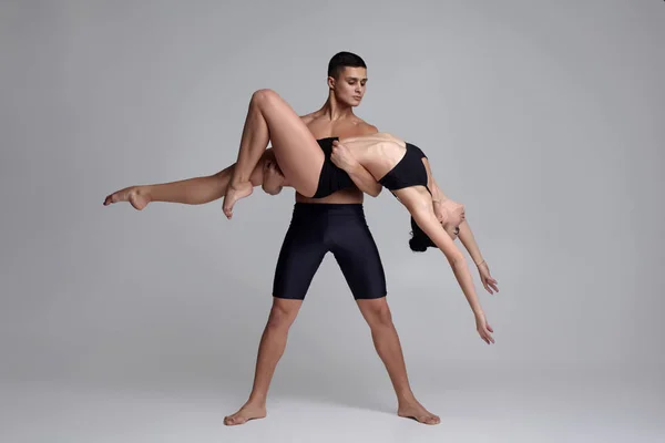 O casal de jovens bailarinos modernos em ternos pretos estão posando sobre um fundo de estúdio cinza . — Fotografia de Stock