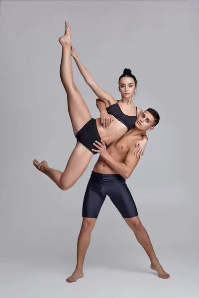 O casal de jovens bailarinos modernos em ternos pretos estão posando sobre um fundo de estúdio cinza . — Fotografia de Stock