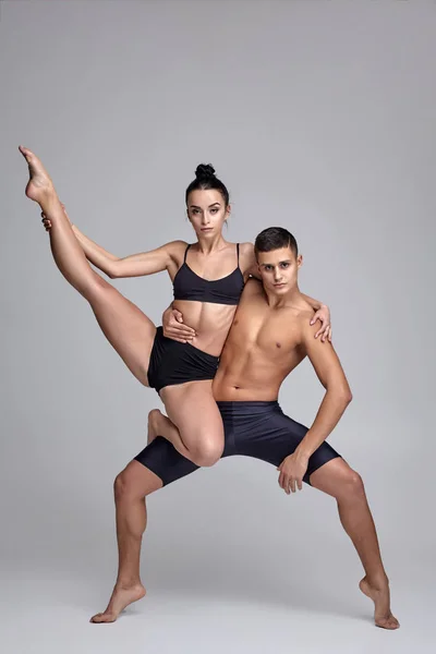 O casal de jovens bailarinos modernos em ternos pretos estão posando sobre um fundo de estúdio cinza . — Fotografia de Stock