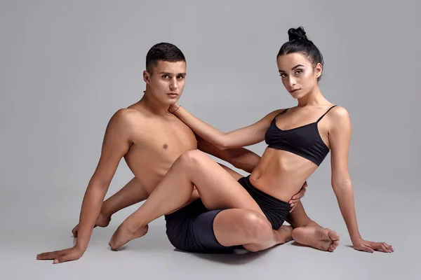 La pareja de jóvenes bailarines de ballet modernos con trajes negros posan sobre un fondo gris de estudio . — Foto de Stock