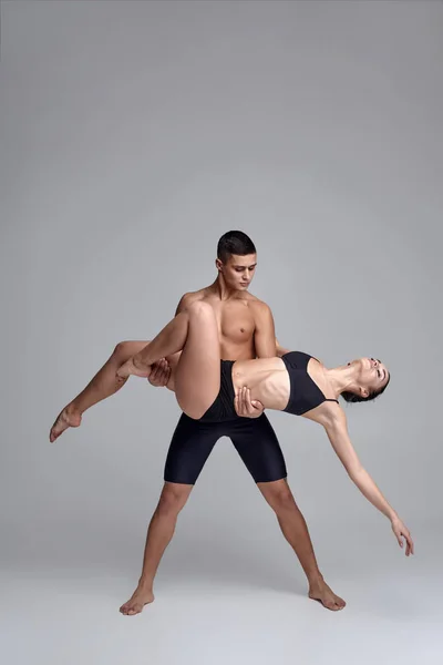 O casal de jovens bailarinos modernos em ternos pretos estão posando sobre um fundo de estúdio cinza . — Fotografia de Stock
