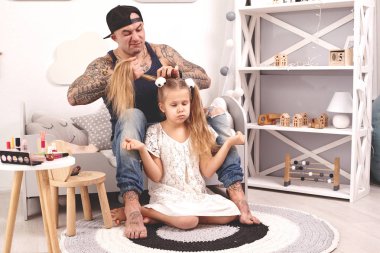 Komik zaman Tattoed baba bir kap ve çocuğu evde oynuyor. Babam kızlarının saçını yatak odasında yapıyor. Aile tatili ve birliktelik