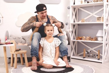 Komik zaman Tattoed baba bir kap ve çocuğu evde oynuyor. Babam kızlarının saçını yatak odasında yapıyor. Aile tatili ve birliktelik