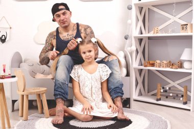 Komik zaman Tattoed baba bir kap ve çocuğu evde oynuyor. Babam kızlarının saçını yatak odasında yapıyor. Aile tatili ve birliktelik