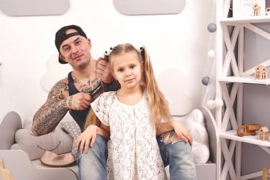 Komik zaman Tattoed baba bir kap ve çocuğu evde oynuyor. Babam kızlarının saçını yatak odasında yapıyor. Aile tatili ve birliktelik