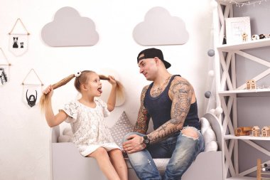 Komik zaman Tattoed baba bir kap ve çocuğu evde oynuyor. Babam kızlarının saçını yatak odasında yapıyor. Aile tatili ve birliktelik