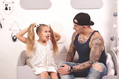 Komik zaman Tattoed baba bir kap ve çocuğu evde oynuyor. Babam kızlarının saçını yatak odasında yapıyor. Aile tatili ve birliktelik