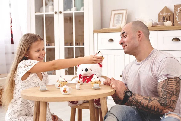 Rozkošná dcera nosí v bílých šatech svůj milující otec. Popíjí čaj z hračiček v moderním dětném pokoji, kde je dřevěný nábytek. Šťastná rodina. — Stock fotografie