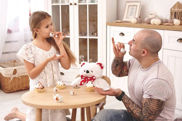 Rozkošná dcera nosí v bílých šatech svůj milující otec. Popíjí čaj z hračkářská jídla v moderním dětovém pokoji. Šťastná rodina. — Stock fotografie